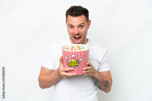 Young caucasian handsome man isolated on white background holding a big bucket of popcorns