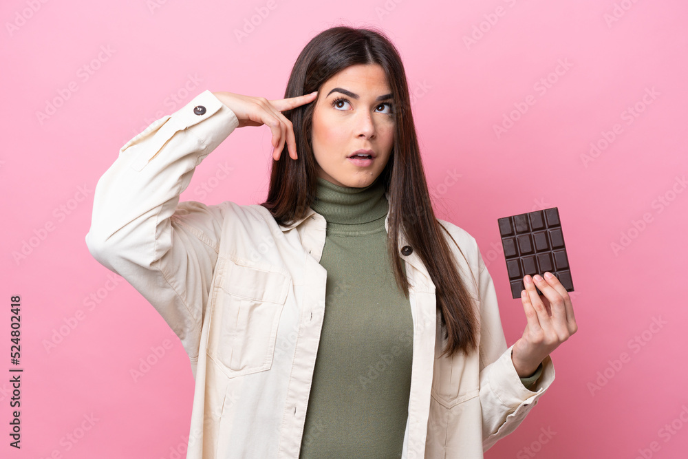 Young Brazilian woman with chocolat isolated on pink background having doubts and thinking Young Brazilian woman with chocolat isolated on pink background having doubts and thinking
