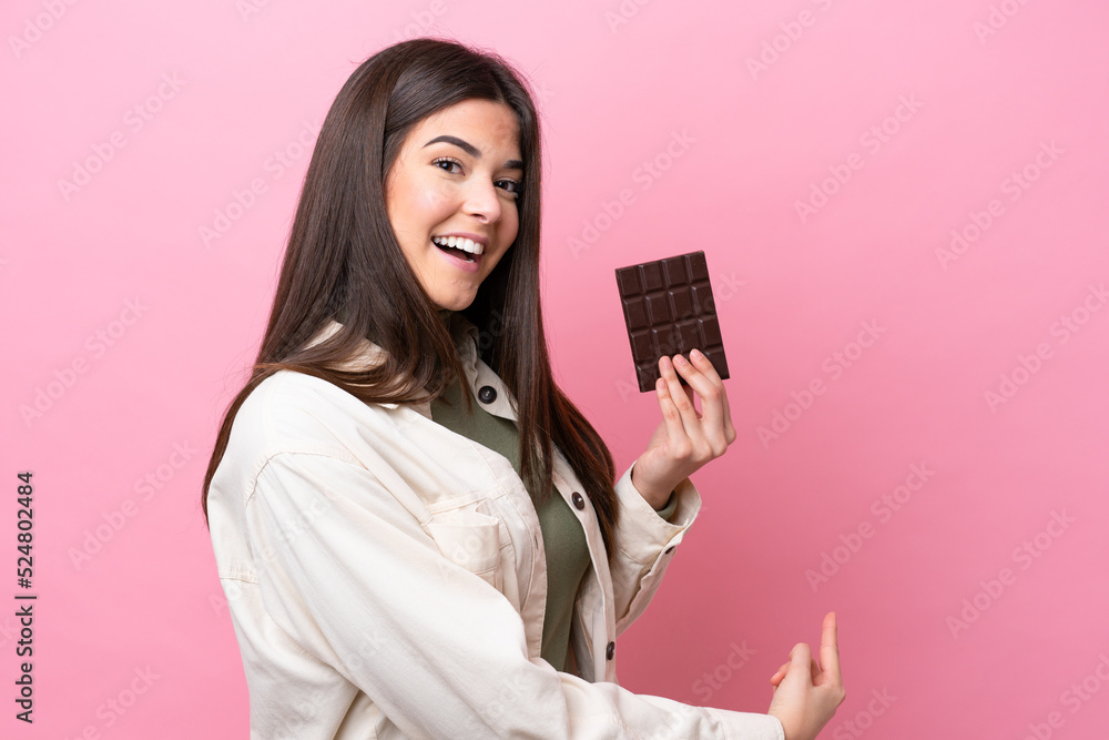 Young Brazilian woman with chocolat isolated on pink background pointing back Young Brazilian woman with chocolat isolated on pink background pointing back