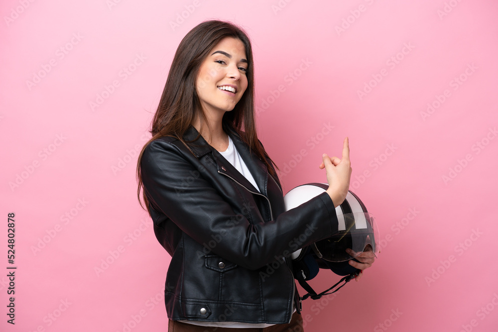 Young Brazilian woman with a motorcycle helmet isolated on pink background pointing back Young Brazilian woman with a motorcycle helmet isolated on pink background pointing back