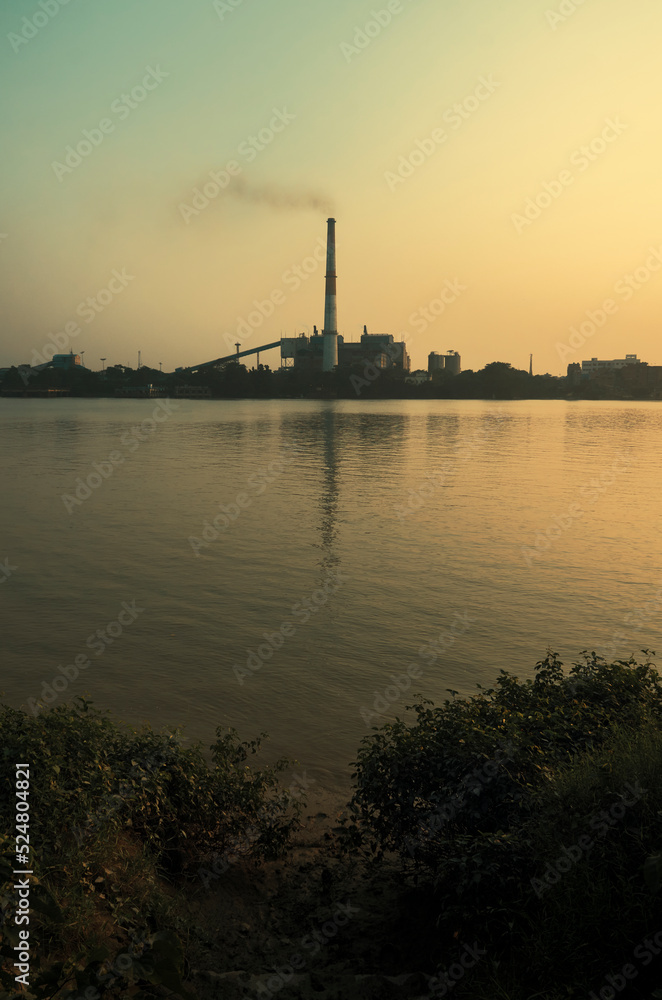Silhouette of factory chimney emitting smoke at a thermal power station beside Ganges river. Photo taken during dusk.