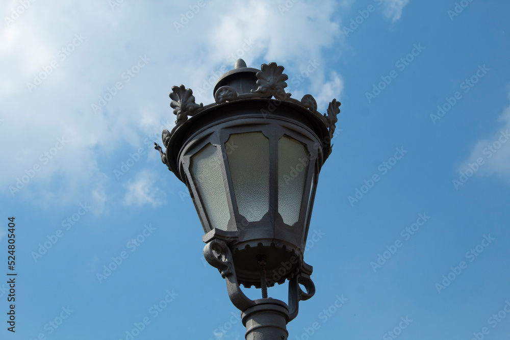 Vintage style street lamp top isolated on blue sky with clouds. Retro european lantern