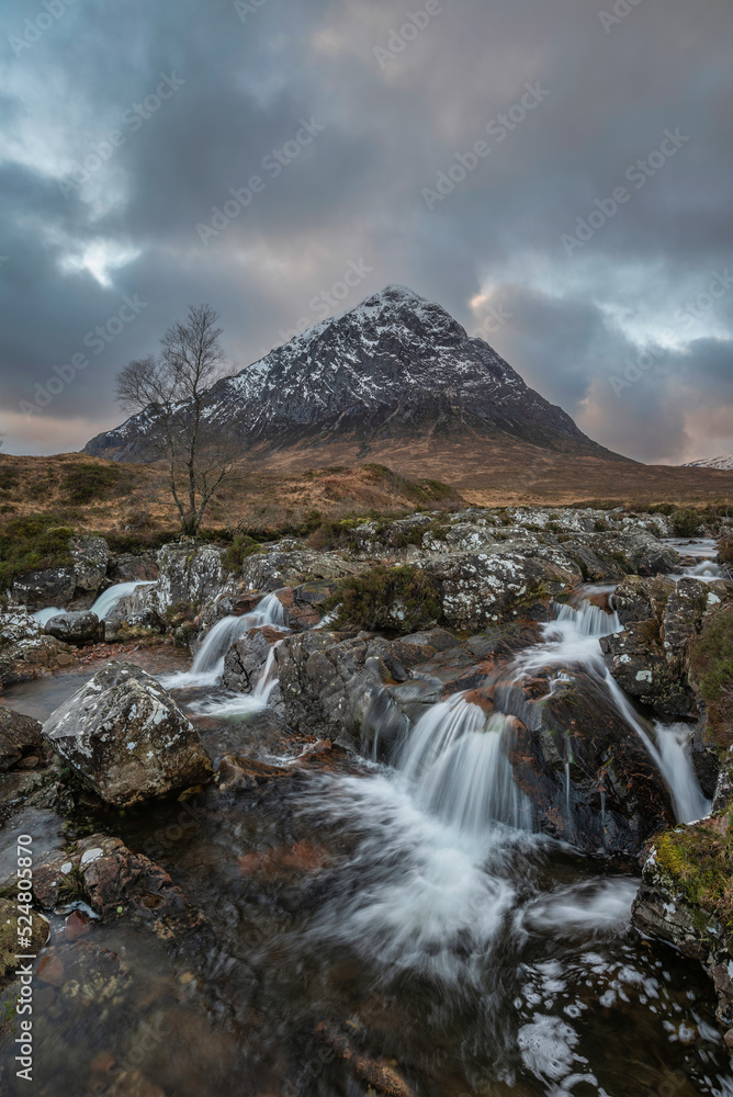Epic majestic Winter sunset landscape of Stob Dearg Buachaille Etive Mor iconic peak in Scottish Highlands with famous River Etive waterfalls in foreground