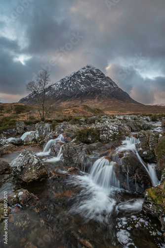 Epic majestic Winter sunset landscape of Stob Dearg Buachaille Etive Mor iconic peak in Scottish Highlands with famous River Etive waterfalls in foreground