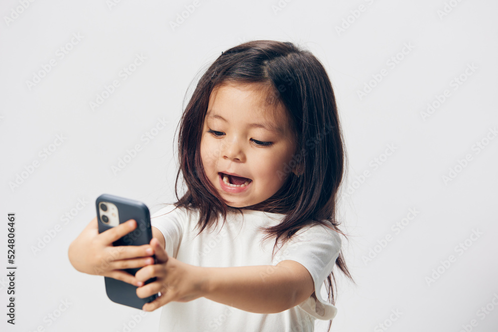 a happy little girl stands with a fashionable smartphone on outstretched arms and looks into her phone smiling pleasantly. Horizontal photo on a light background with space for mockup a happy little girl stands with a fashionable smartphone on outstretched arms and looks into her phone smiling pleasantly. Horizontal photo on a light background with space for mockup