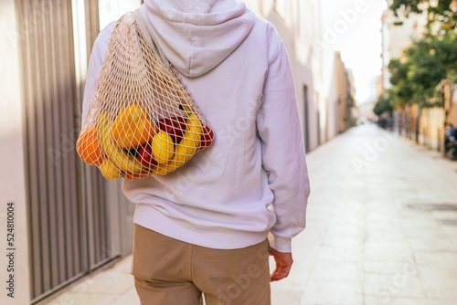 Unrecognizable man walking with groceries in mesh bag photo