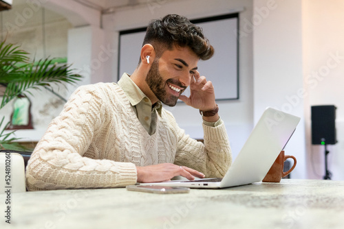 Smiling young ethnic man working distantly on netbook at home photo