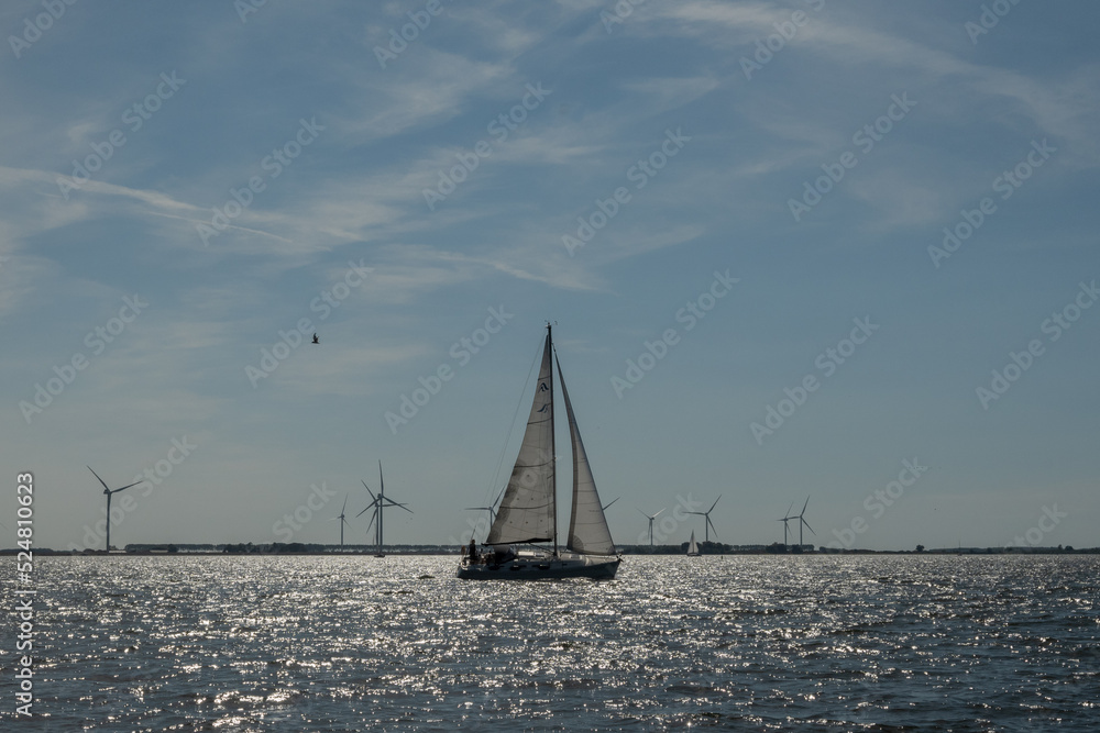 The power of wind. a sail boat in the foreground propelled on the water by wild in the same way as the turbines in the background generate clear sustainable power for public usage