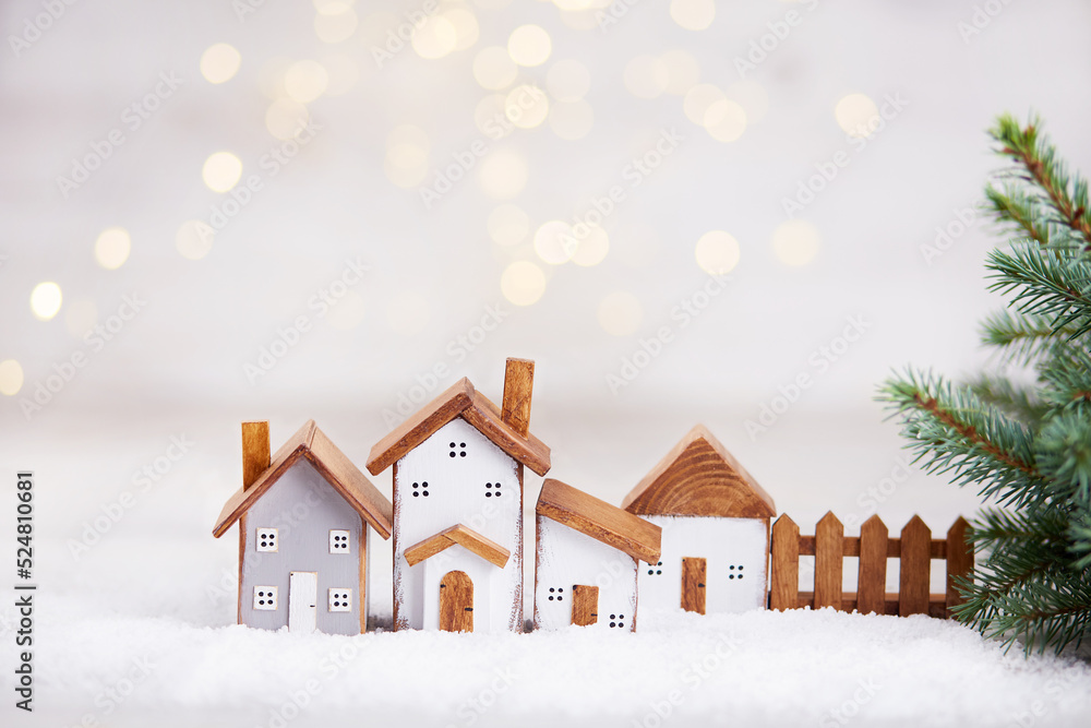 Happy New Year and Merry Christmas greeting card. Toy wooden houses, spruce branches on the background of a beautiful bokeh. 