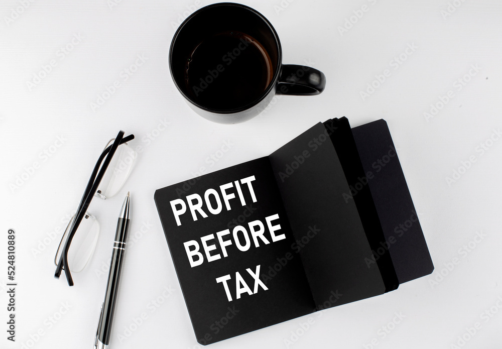 PROFIT BEFORE TAX written text in small black notebook with coffee , pen and glasess on a white background. Black-white style PROFIT BEFORE TAX written text in small black notebook with coffee , pen and glasess on a white background. Black-white style