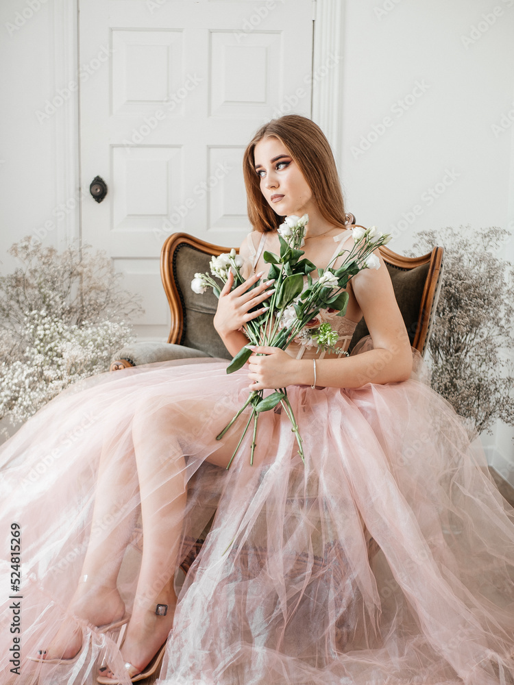 A girl with voluminous hair poses in a pink dress with flowers in her hands