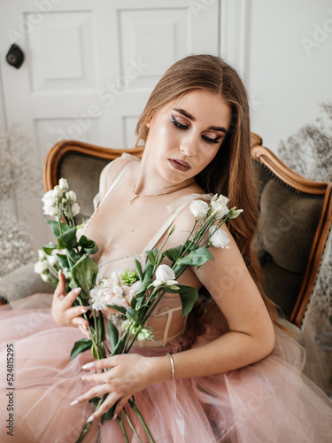 Obraz na płótnie A girl with voluminous hair poses in a pink dress with flowers in her hands w salonie