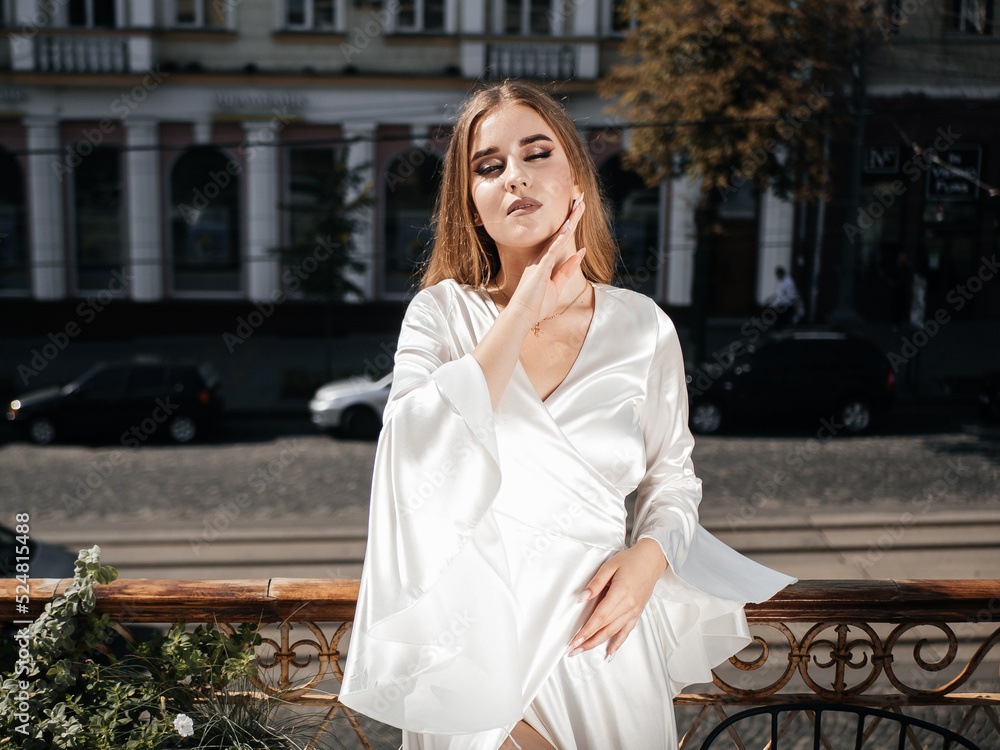 A girl in a white dress poses on the balcony