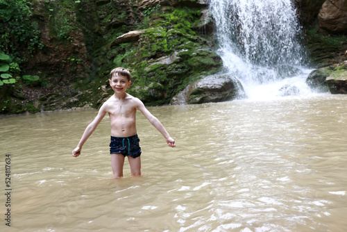 Fototapeta Naklejka Na Ścianę i Meble -  Child posing in Rufabgo stream next to waterfall Shum