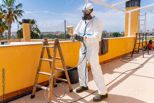 Male worker with aerograph renovating house photo