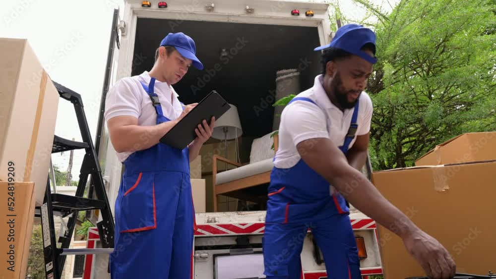 Two delivery men carrying and checking cardboard box in new home Two delivery men carrying and checking cardboard box in new home