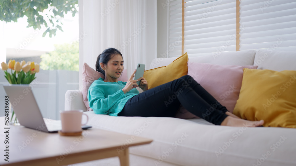 Young attractive beautiful casual asia female lady or student look at cellphone play social media IG reel tiktok app lying down at sofa couch living room feel relax comfort carefree at home apartment. Young attractive beautiful casual asia female lady or student look at cellphone play social media IG reel tiktok app lying down at sofa couch living room feel relax comfort carefree at home apartment.
