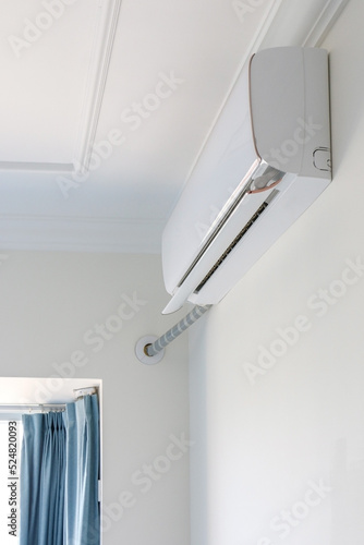 Air conditioner on top of white wall turned on, cooling down room interior during heat wave