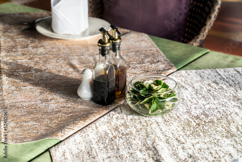 A condiment set is set on the wooden table with the shadow of the bottle lay down on the table cloth.