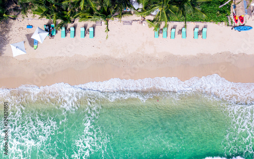 A bird-eye-view of an island with a row beach bed situated on white sand beach and the view of white wave and turquoise-color sea water