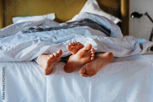 Anonymous couple cuddling feet while sleeping together under blanket
