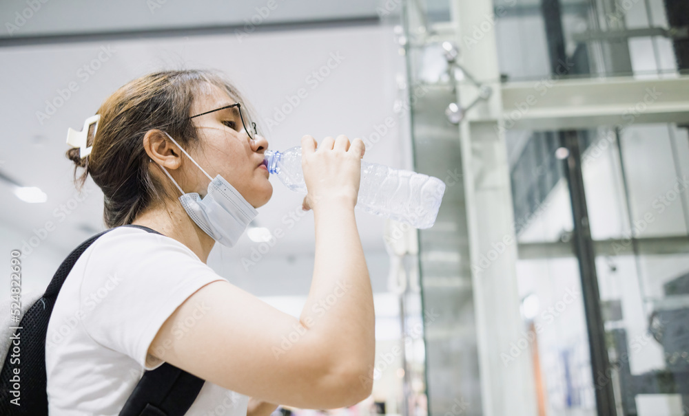 Asian woman drinking from a plastic water bottle. Wear a mask under her chin. Asian woman drinking from a plastic water bottle. Wear a mask under her chin.