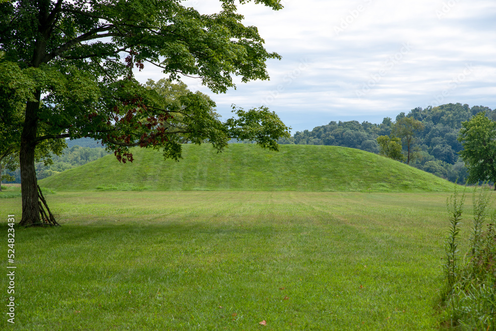 Large Native American prehistoric earthwork burial mound at Seip Earthworks, Ohio. Dramatic sky and freshly mowed green grass with woodland background and long ancient burial mound.