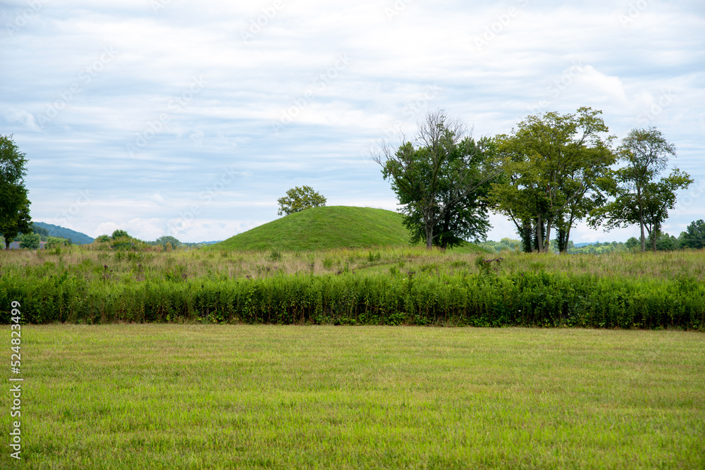 Prehistoric Native North American earthen burial mound seen from grass area in meadow. Large Native American prehistoric earthwork burial mound at Seip Earthworks, Ohio. Dramatic sky and mowed grass.