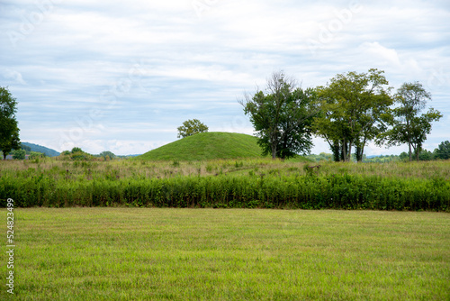 Prehistoric Native North American earthen burial mound seen from grass area in meadow. Large Native American prehistoric earthwork burial mound at Seip Earthworks, Ohio. Dramatic sky and mowed grass. photo
