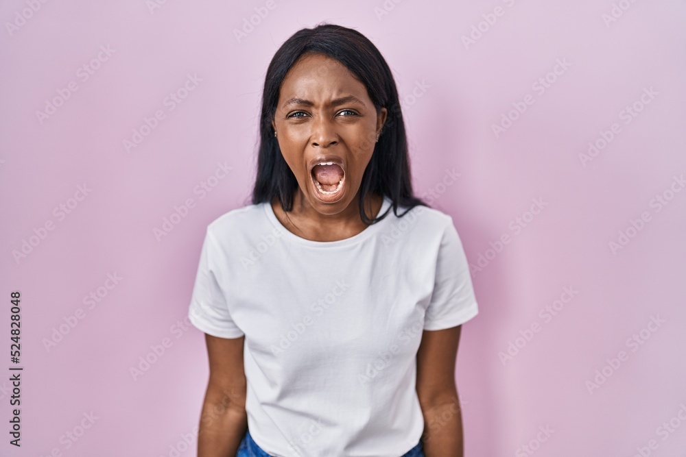 Fototapeta premium African young woman wearing casual white t shirt angry and mad screaming frustrated and furious, shouting with anger. rage and aggressive concept.