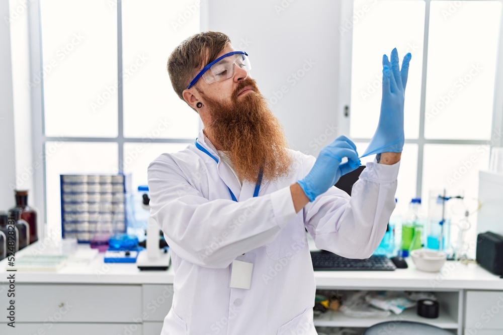 Young redhead man wearing scientist uniform wearing gloves at laboratory Young redhead man wearing scientist uniform wearing gloves at laboratory
