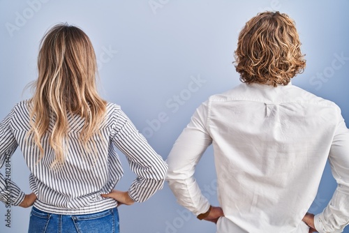 Young couple standing over blue background standing backwards looking away with arms on body