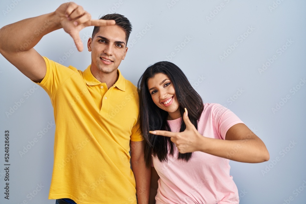 Young couple standing over isolated background smiling making frame with hands and fingers with happy face. creativity and photography concept. Young couple standing over isolated background smiling making frame with hands and fingers with happy face. creativity and photography concept.