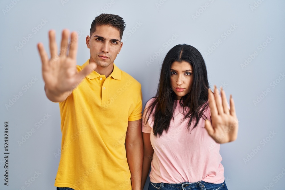 Young couple standing over isolated background doing stop sing with palm of the hand. warning expression with negative and serious gesture on the face. Young couple standing over isolated background doing stop sing with palm of the hand. warning expression with negative and serious gesture on the face.
