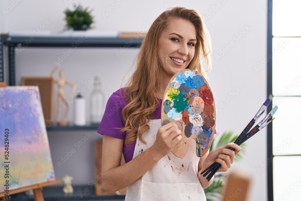 Young blonde woman artist smiling confident holding paintbrushes and palette at art studio Young blonde woman artist smiling confident holding paintbrushes and palette at art studio