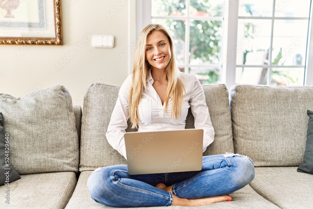 Young blonde woman using laptop sitting on the sofa at home. Young blonde woman using laptop sitting on the sofa at home.