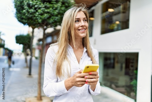 Beautiful blonde woman smiling happy outdoors on a sunny day using smartphone