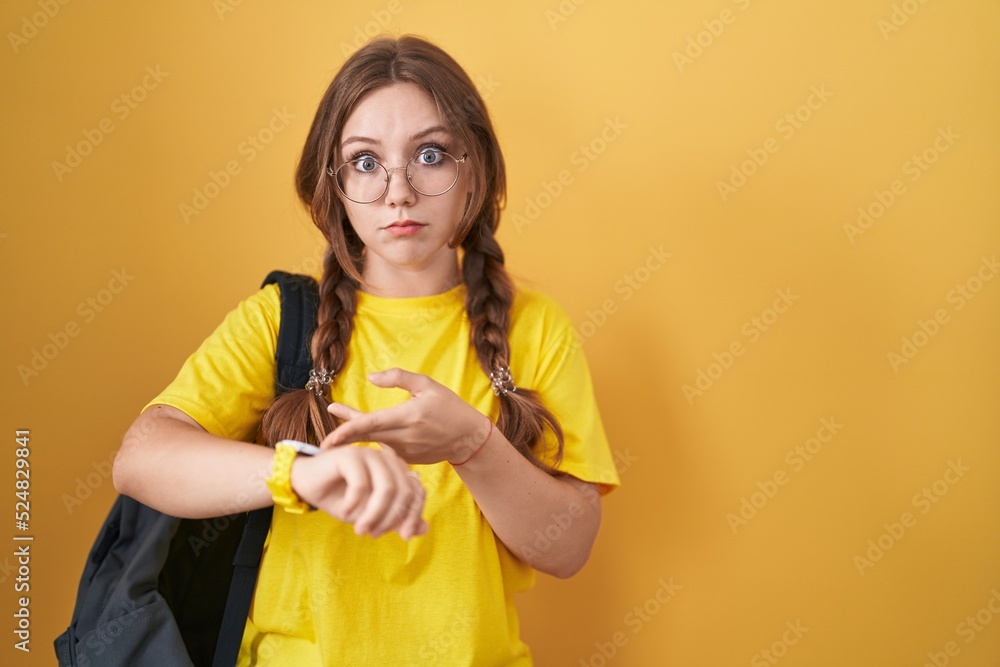 Young caucasian woman wearing student backpack over yellow background in hurry pointing to watch time, impatience, upset and angry for deadline delay Young caucasian woman wearing student backpack over yellow background in hurry pointing to watch time, impatience, upset and angry for deadline delay