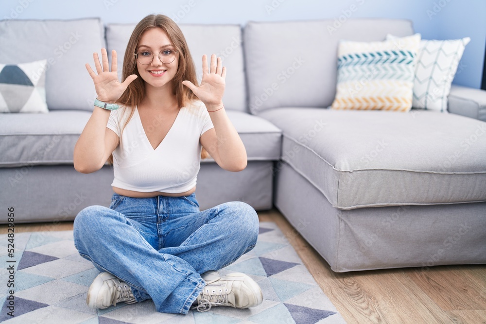 Young caucasian woman sitting on the floor at the living room showing and pointing up with fingers number ten while smiling confident and happy. Young caucasian woman sitting on the floor at the living room showing and pointing up with fingers number ten while smiling confident and happy.