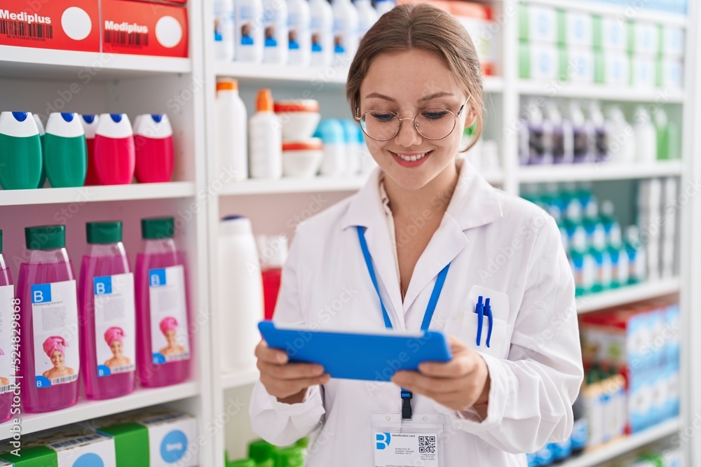 Young blonde woman pharmacist using touchpad working at pharmacy