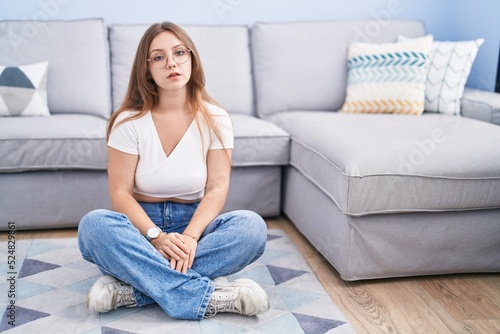 Young caucasian woman sitting on the floor at the living room looking sleepy and tired, exhausted for fatigue and hangover, lazy eyes in the morning.