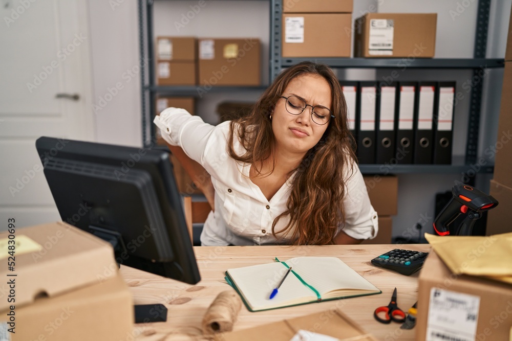 Young hispanic woman working at small business ecommerce suffering of backache, touching back with hand, muscular pain Young hispanic woman working at small business ecommerce suffering of backache, touching back with hand, muscular pain