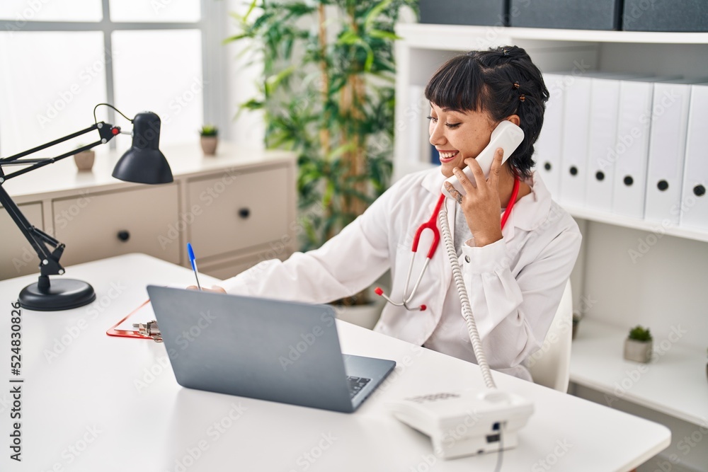Young woman wearing doctor uniform talking on the telephone at clinic Young woman wearing doctor uniform talking on the telephone at clinic