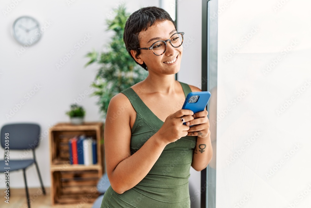 Young hispanic woman smiling confident using smartphone standing at waiting room Young hispanic woman smiling confident using smartphone standing at waiting room
