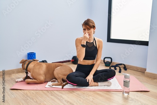 Young beautiful woman sitting on yoga mat smelling something stinky and disgusting, intolerable smell, holding breath with fingers on nose. bad smell