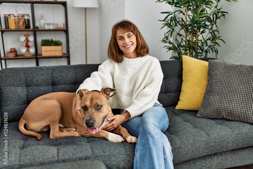 Young caucasian woman smiling confident hugging dog sitting on sofa at home