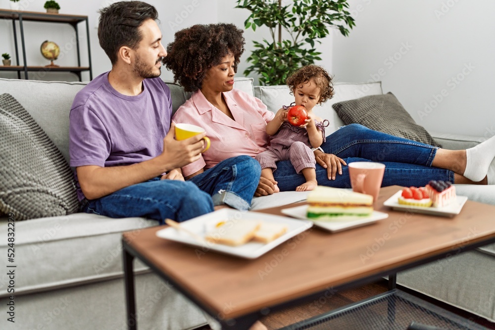 Couple and daughter having breakfast sitting on sofa at home Couple and daughter having breakfast sitting on sofa at home