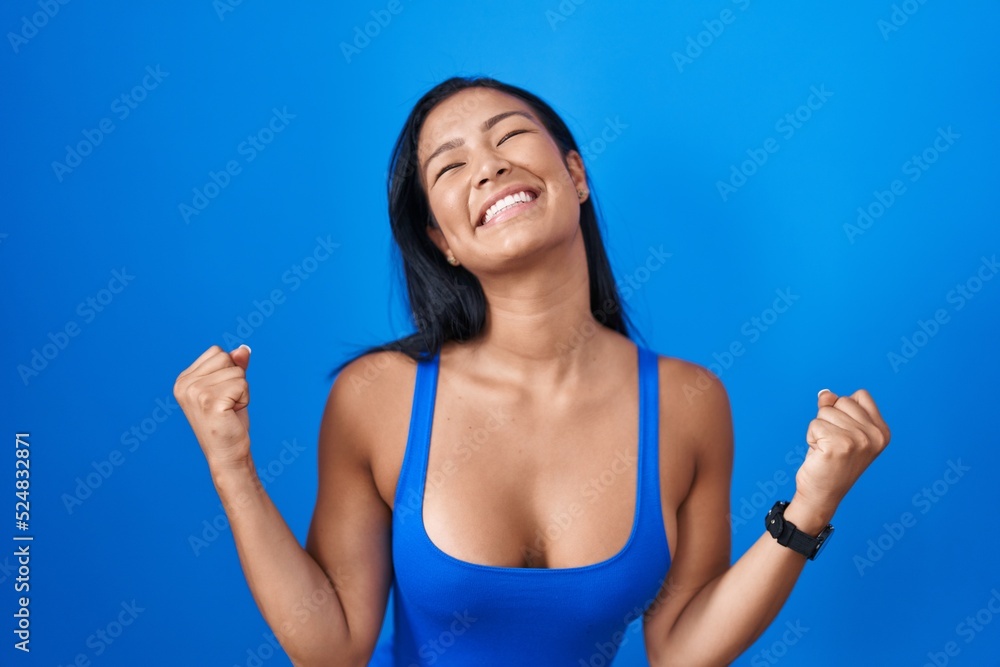 Hispanic woman standing over blue background celebrating surprised and amazed for success with arms raised and eyes closed. winner concept. Hispanic woman standing over blue background celebrating surprised and amazed for success with arms raised and eyes closed. winner concept.