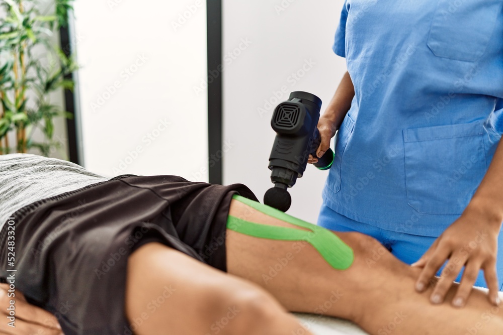 Young latin physioterapist woman make rehab treatment to hispanic man using massage gun percusion tool at the clinic.