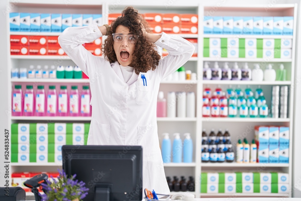 Φωτογραφία Hispanic woman with curly hair working at pharmacy drugstore crazy and scared wi